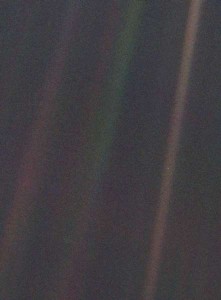 Earth appears as a tiny dot, the blueish-white speck approximately halfway down the brown band to the right